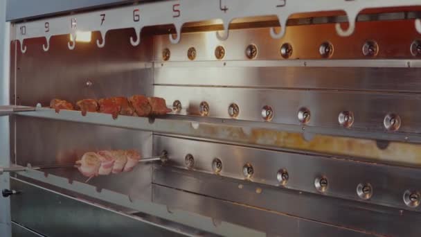 La carne está girando dentro de chargrill en el restaurante, cocinero está poniendo patas de pollo — Vídeo de stock