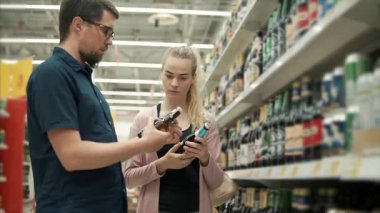 Genç çift bir süpermarkette alkol departmanında duruyor, bira satın alıyor.
