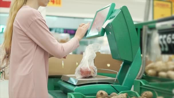 Vrouwelijke shopper weegt groenten op een schaal in een supermarkt — Stockvideo