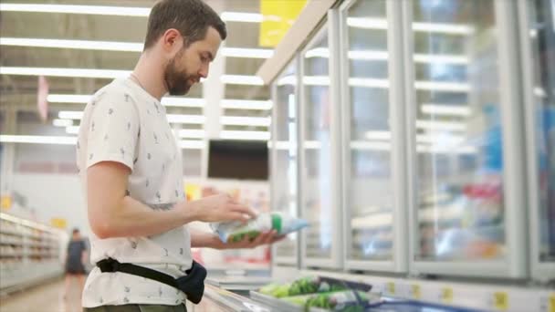 Jeune homme examine paquet avec des légumes surgelés dans une salle de supermarché — Video