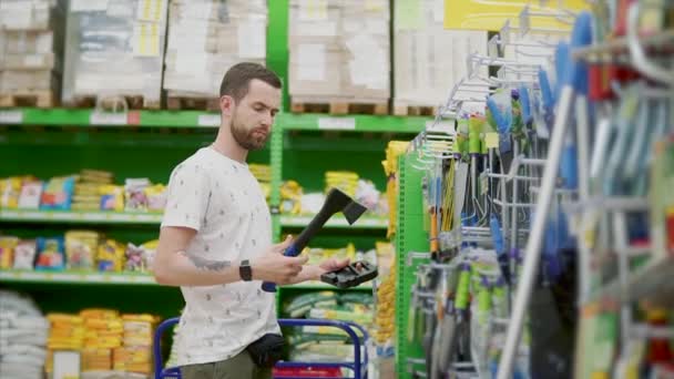 L'homme adulte prend la hache dans un magasin, l'inspecte et la remet sur support — Video