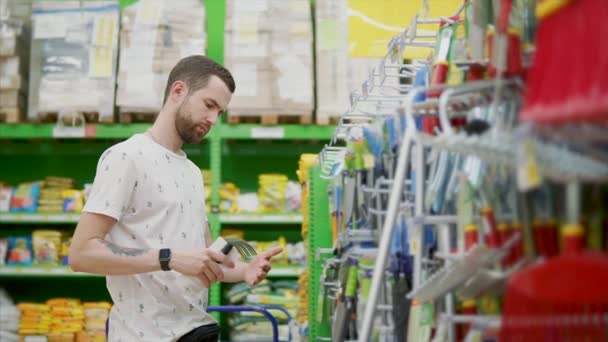 Homem de cabelos escuros está inspecionando ferramentas para trabalhos de jardim em um hipermercado — Vídeo de Stock