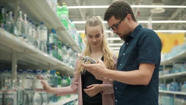 Los cónyuges están leyendo etiquetas en botellas de agua en una tienda — Vídeo de stock