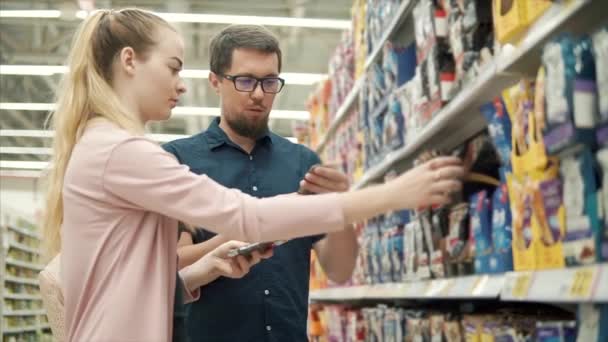 Adulto homem e mulher estão tomando pacotes com animais de estimação forragem em um supermercado — Vídeo de Stock