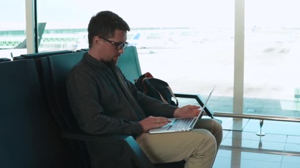 Hombre de negocios adulto está escribiendo en un ordenador portátil sentado en la sala del aeropuerto — Vídeo de stock