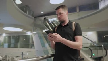 Genç adam modern binaların salonda elinde tutan Smartphone kullanıyor