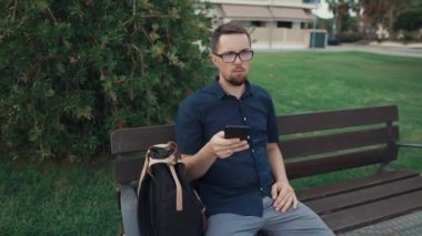 Sakallı adam akıllı telefonda tarama, gündüz bankta rahatlatıcı