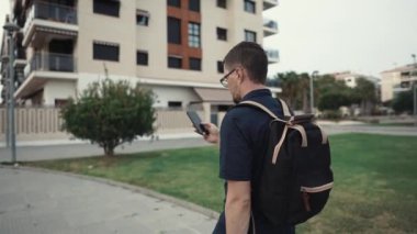 Sırt çantası ve telefon ile öğrenci adam binaya yakın bahçesinde yürüyor, arka görünüm