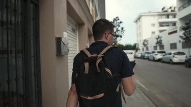 Yalnız adam yaz gününde şehir binaları ve yollar boyunca yürüyor, arka görünüm