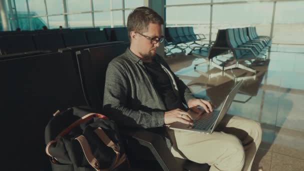 Ensam manlig passagerare väntar sitt flyg i en Terminal och surfar i laptop — Stockvideo