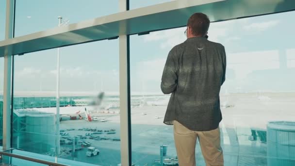 De volwassen mens spreekt door mobiele telefoon in Terminal van luchthaven, achter mening — Stockvideo