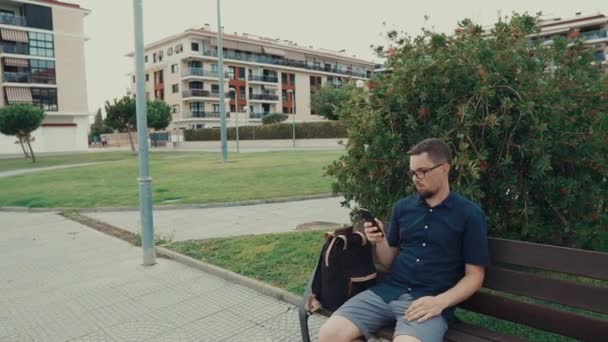 Jeune homme assis sur un banc dans un parc . — Video