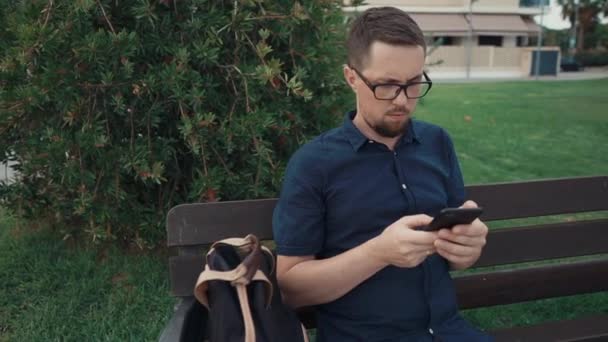 스마트폰을 사용하여 벤치에 앉아 있는 남자. — 비디오