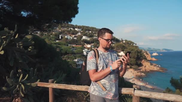 Adult townsman is standing in background of sea coastline, using smartphone — Stock Video