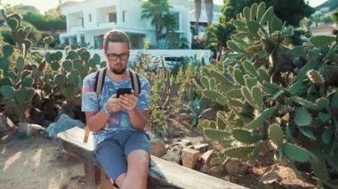 Adam güneşli akşam Bahçe parkında bir bankta oturuyor, Smartphone kullanarak