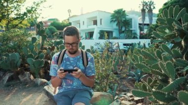 Sakallı adam yaz gününde parkta dinleniyor, tezgah üzerinde oturuyor ve telefonda oynuyor