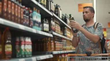 Genç adam raf şişe alarak, bir bakkal içinde zeytin yağı seçiyor