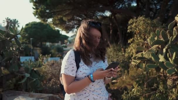 Mujer joven está sentado en el banco en el jardín por la noche, jugando con el teléfono móvil — Vídeo de stock