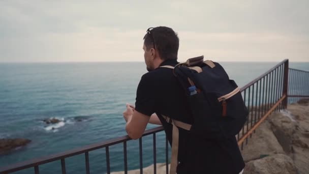 Sorrowful adult man is watching alone on ocean view in evening time from rock — Stock Video