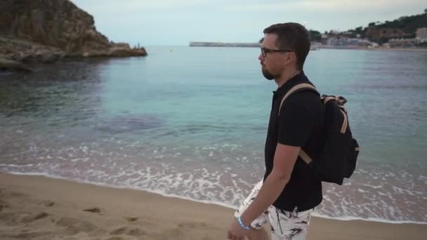 Человек наслаждается одинокой прогулкой по песчаному пляжу в сумерках возле морской воды — стоковое видео
