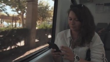 Yetişkin esmer kadın, SMS gönderme, trende oturan akıllı telefon tarafından sohbet ediyor