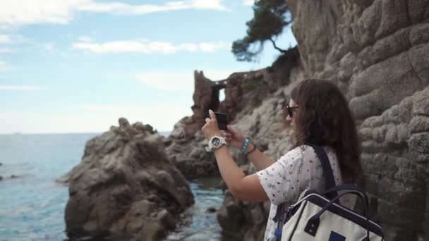 Mujer tomando fotos de un mar y rocas . — Vídeos de Stock