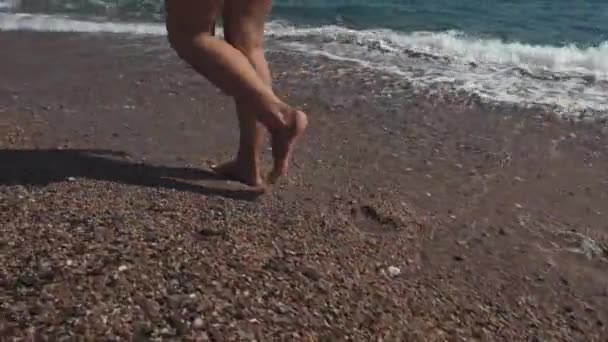 Mujer está paseando sola en una orilla del mar en un día soleado, primer plano de sus piernas — Vídeos de Stock