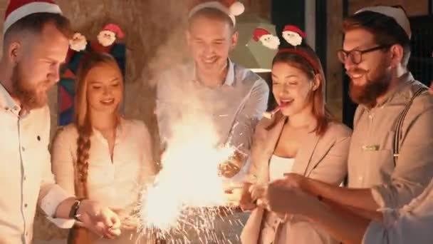 Los jóvenes felices están encendiendo chispas en la noche de Navidad en la fiesta y animando — Vídeos de Stock