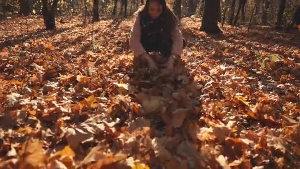 Heranwachsendes Mädchen spielt im Wald mit trockenem Laub und wirft sich in die Luft — Stockvideo