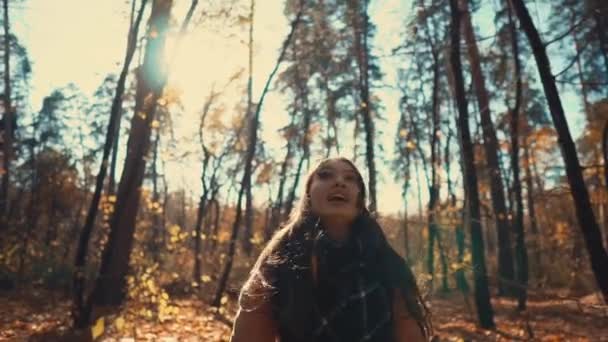 Feliz joven mujer está lanzando hojas y girando alegremente en el bosque de otoño — Vídeo de stock