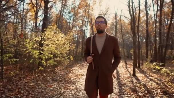 Hombre guapo con gafas paseando en el bosque de otoño durante el día, mirando a su alrededor — Vídeos de Stock