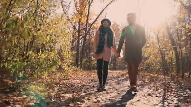 Молодая супружеская пара гуляет в осеннем парке, между голыми деревьями — стоковое видео
