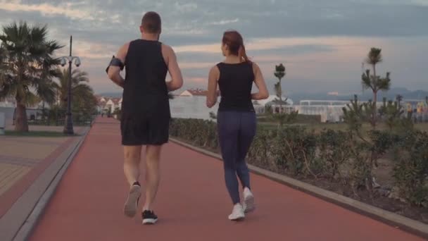 Paire de gars et de filles sportives font du jogging dans la zone du parc le soir, vue arrière — Video