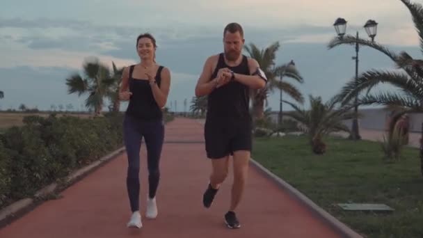 Pareja feliz de deportistas están corriendo en la zona del parque en el crepúsculo, hombre y mujer — Vídeo de stock