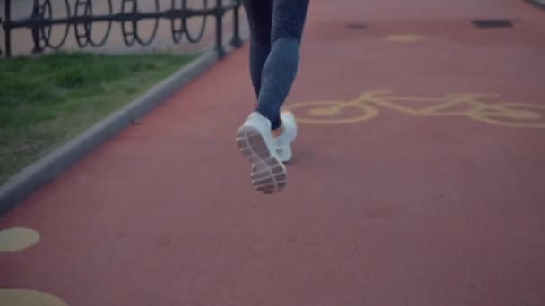 Joven deportista delgado está trotando solo en la noche sobre un camino especial, vista trasera — Vídeo de stock