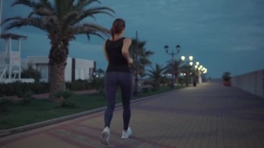 Genç ince sporcu olduğunu jogging içinde gece zaman içinde şehir Embankment, arka görünüm
