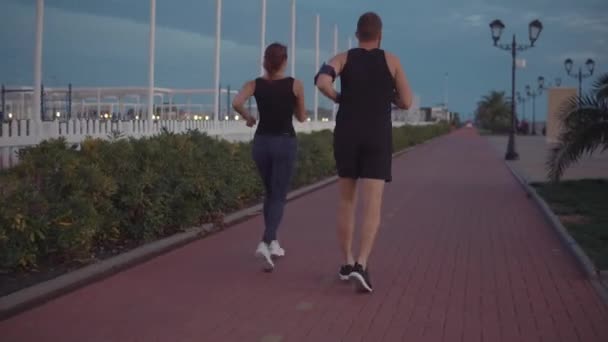 El hombre con su novia están trotando juntos en el área deportiva, charlando felizmente — Vídeo de stock