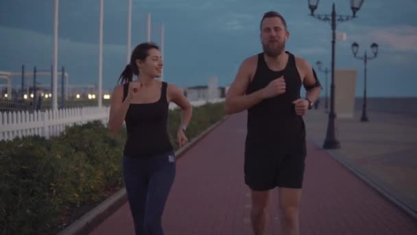 Homem e mulher corredores estão flertando durante a noite correndo ao ar livre, rostos felizes — Vídeo de Stock