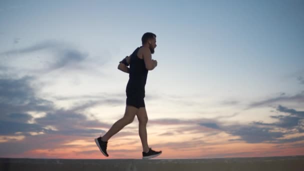 Adulto corredor masculino está corriendo contra el cielo nublado en la hora de la puesta del sol — Vídeos de Stock