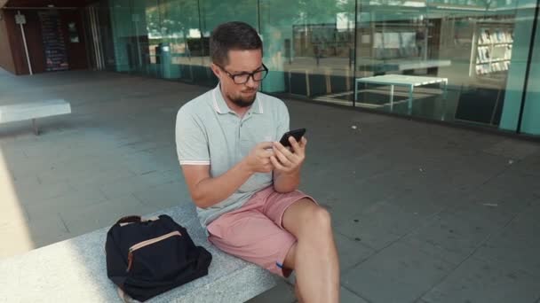 Facet siedzi ze smartfonem na zewnątrz. — Wideo stockowe