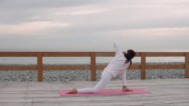 Sportswoman Yoga Asanas değişiyor, katta oturan, deniz manzaralı arka planda