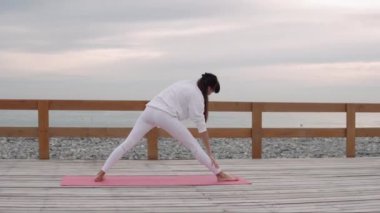 Kadın jimnastikçi deniz yakınında yaz gününde açık havada Trikonasana performans