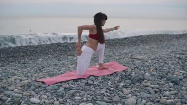 Kadın jimnastikçi deniz kıyısında kaslar ve tendonlar germe, yoga pratik
