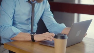 Genç işadamı ofiste laptop klavyede yazarak ve kahve alarak