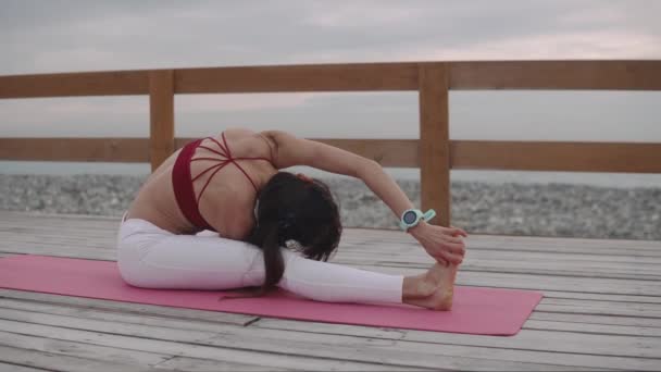 Женщина растягивает ноги делая физические упражнения на открытом воздухе, сидя на полу — стоковое видео