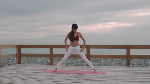 Mujer morena se inclina hacia adelante y hacia abajo, haciendo ejercicio de yoga al aire libre — Vídeos de Stock