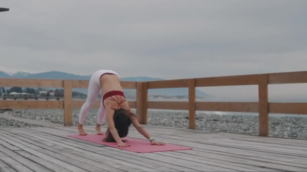 Mujer entrenador de yoga está mostrando posiciones, de pie fuera cerca de la costa — Vídeos de Stock