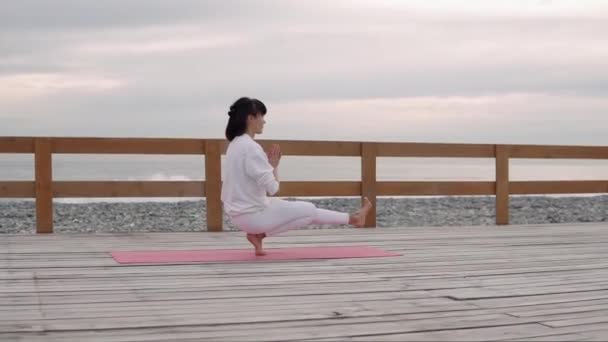 Donna sta mantenendo l'equilibrio seduto su un piede e tenendo il corpo, classe di yoga — Video Stock