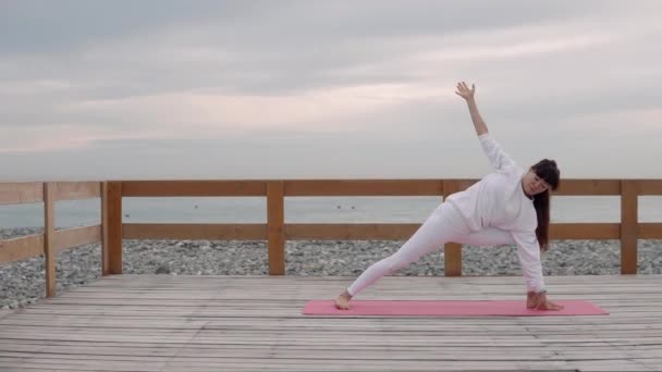 Stark kvinna gör yoga positioner, lutande händer på golvet, Seacoast bakom — Stockvideo