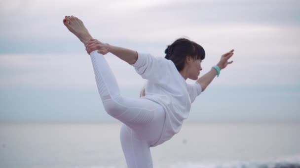 Schlanke Frau hält das Gleichgewicht des Körpers, steht auf einem Bein, Yoga-Praxis — Stockvideo